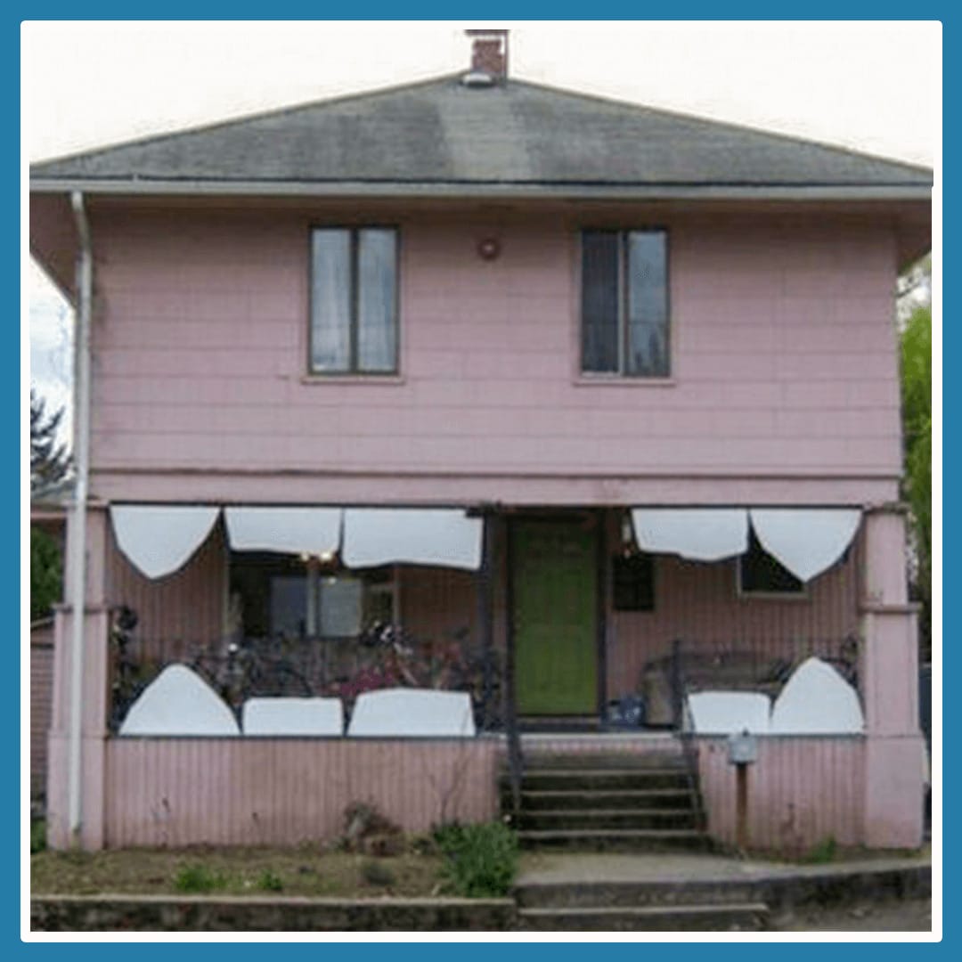 A Pink house that with some odd deck curtains looks like it has funny white teeth and the windows are the eyes.