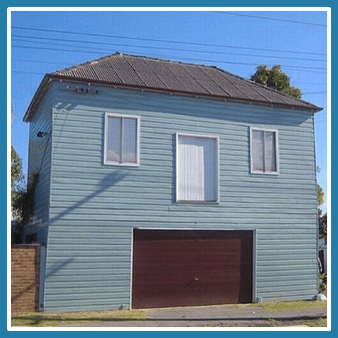 A blue house that looks lt has a big mouth due to the red garage door and window location.